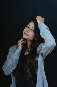 Portrait of young woman standing against black background