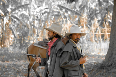 Male friends wearing hats holding guns in forest