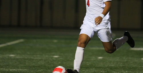 A man kicking a soccer ball on a field at night under the lights.