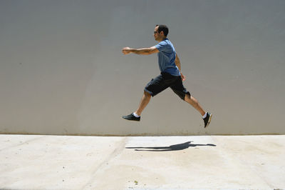 Side view of man levitating over sidewalk by wall