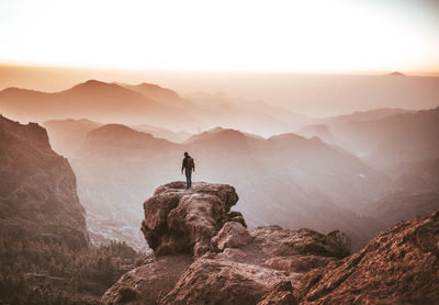 Rear view of man standing on cliff against sky