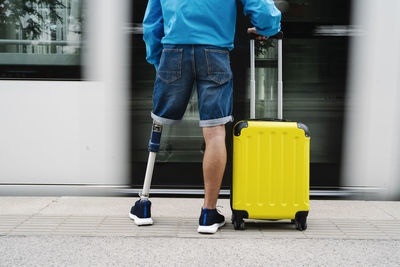 Young man with artificial limb and foot standing by luggage at railroad station