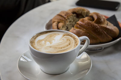 Close-up of cappuccino and croissant served on table