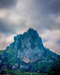 Low angle view of rocky mountain against cloudy sky