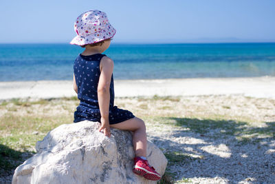 Rear view of girl sitting on rock at beach