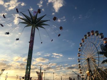Low angle view of ferris wheel and chain swing ride against sky during sunset