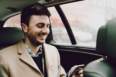 Close-up of happy businessman using phone while traveling in car