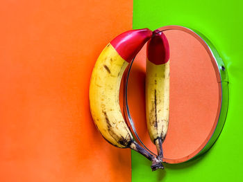 High angle view of red tipped banana on mirror on orange and green background.