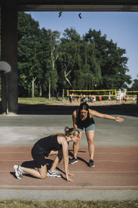 Female coach assisting woman kneeling on running track