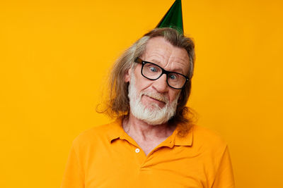 Senior man wearing party hat against yellow background