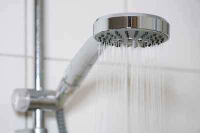 Shower with modern showerhead and running water in domestic bathroom close-up