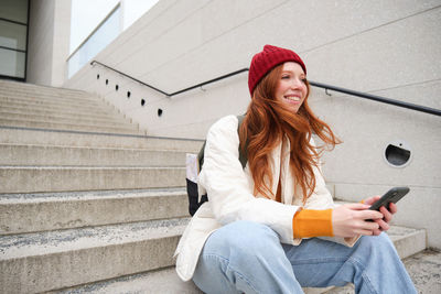 Young woman using mobile phone while sitting on staircase