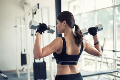 Rear view of woman lifting dumbbells in gym