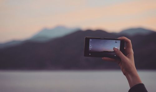 Midsection of person using mobile phone against sky