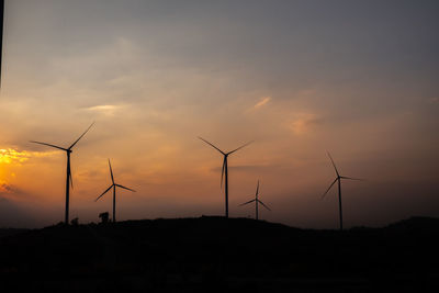 Silhouette wind turbines on land against sky during sunset