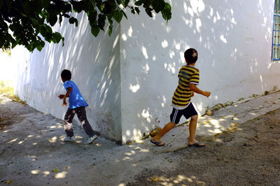 Boys running on footpath by house wall