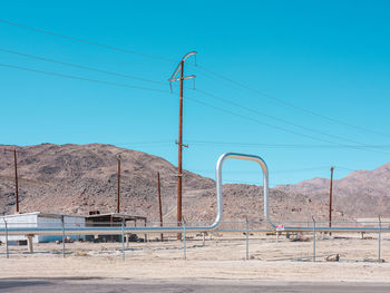 Electricity pylon by road against clear blue sky