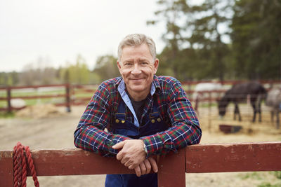 Portrait of smiling mature farmer leaning on fence