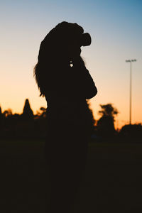 Silhouette woman photographing on field against sky during sunset