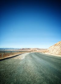 Road amidst field against clear blue sky