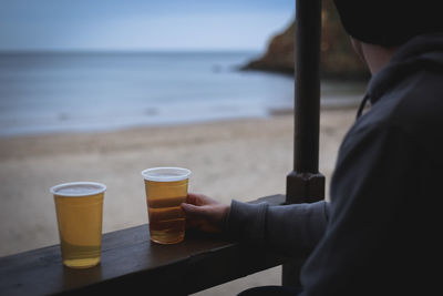 Midsection of man holding beer glass at beach