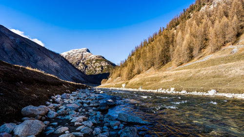 Scenic view of stream amidst snowcapped mountains against blue sky