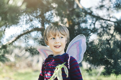 Happy boy in fairy wings looking away at yard