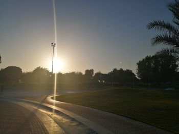 Street amidst field against clear sky during sunset
