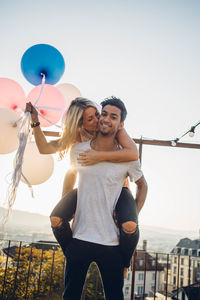 Portrait of a smiling young woman with balloons against sky