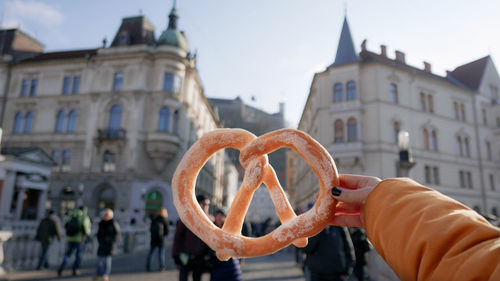 Hand holding pretzel against building in city.