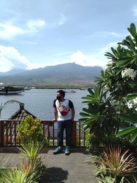 Young man standing at riverbank against sky