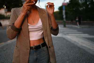 Midsection of woman smoking cigarette while standing outdoors