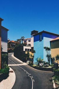 Buildings by empty road against clear blue sky in town