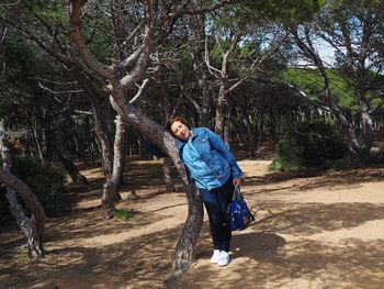 Mature woman leaning on tree trunk in forest