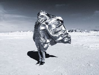 Man covered with silver fabric standing on barren field