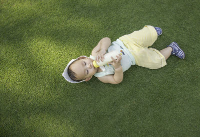 High angle view of child drinking milk while lying on grass