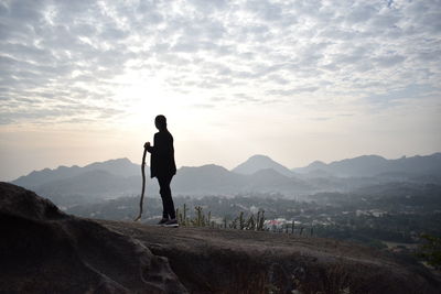 Woman holding stick while standing on landscape against sky during sunset