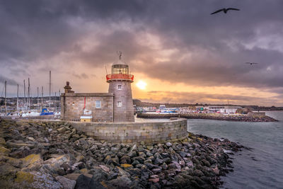 Lighthouse by sea against sky during sunset