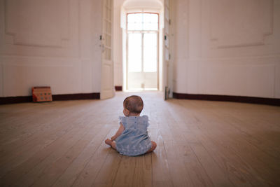 Rear view of girl sitting on hardwood floor