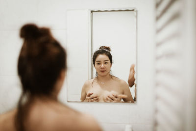 Portrait of woman holding breasts while looking in mirror