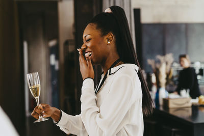 Side view of happy businesswoman laughing while holding drink glass during event at convention center