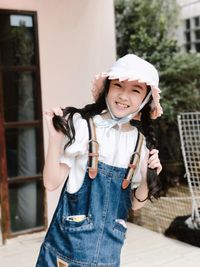 Portrait of smiling girl wearing hat against house