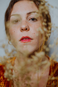 Close-up portrait of young woman seen through dried plant