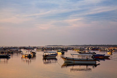 Boats moored in harbor at sunset