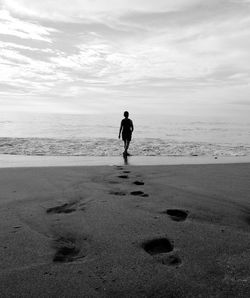 Rear view of man walking at beach against sky