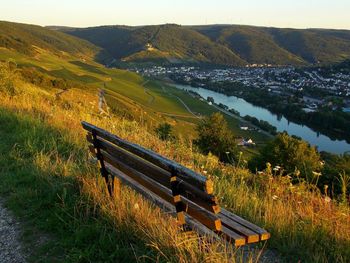 Empty bench on field by mountains against sky