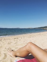 Low section of woman on beach against clear blue sky