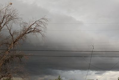 Low angle view of electricity pylon against cloudy sky