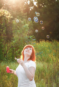 Side view of young woman blowing bubbles on field