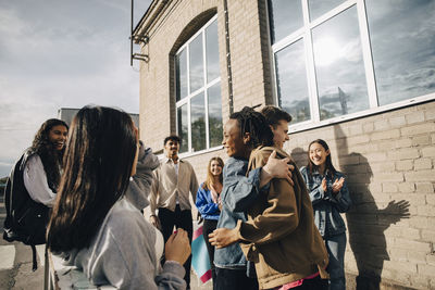 Smiling young man embracing woman by friends outside building